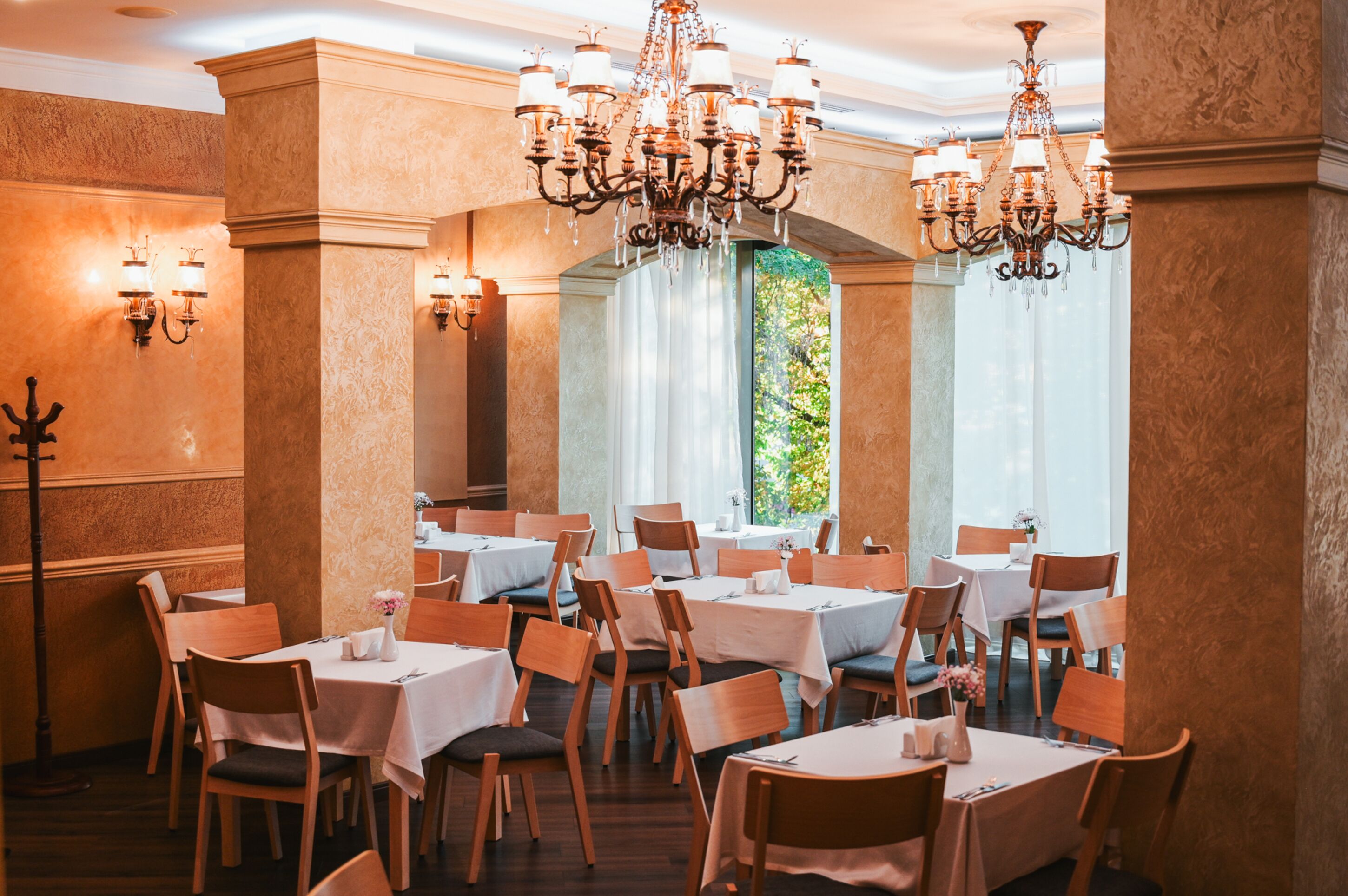 A restaurant with multiple tables and chairs, chandeliers, and wall sconces.