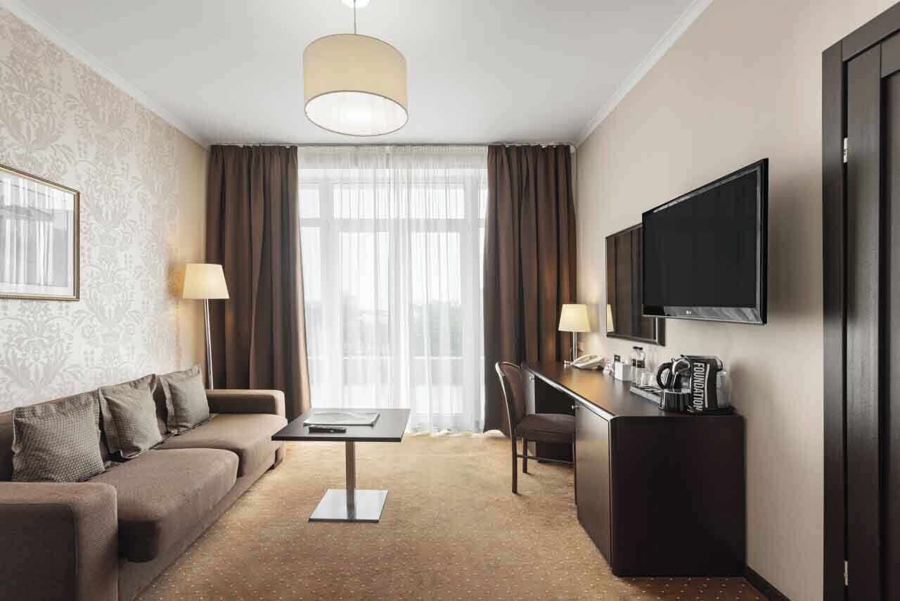 A hotel room with a sofa, a desk, a television, and a window with curtains.