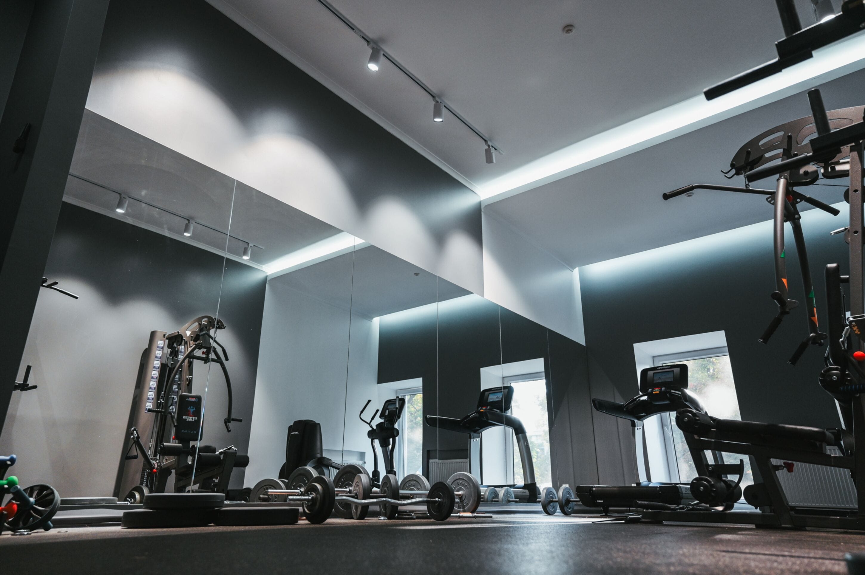 A modern gym with various exercise equipment, large windows, and a minimalist design.