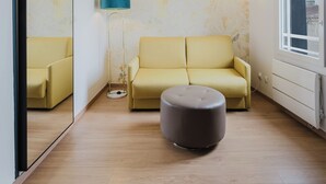 A modern living room with a yellow sofa, a round ottoman, a floor lamp, and a large mirror. - Hôtel Amaya (Ambares-et-Lagrave)