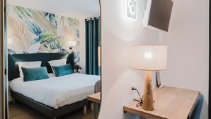 A hotel room with a bed, a desk, a chair, a mirror, a TV, and a lamp. - Hôtel Amaya (Ambares-et-Lagrave)