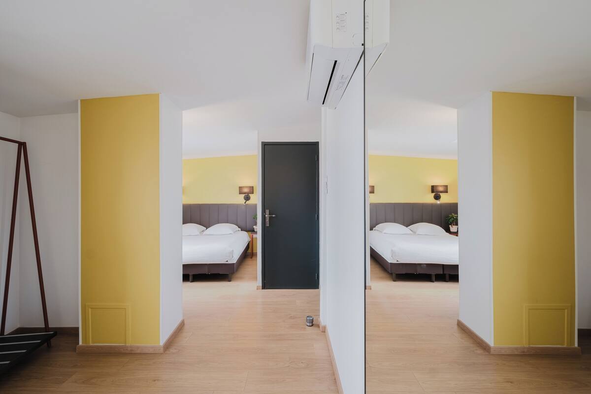 A hotel room with two beds, a door, and a small table with a lamp.