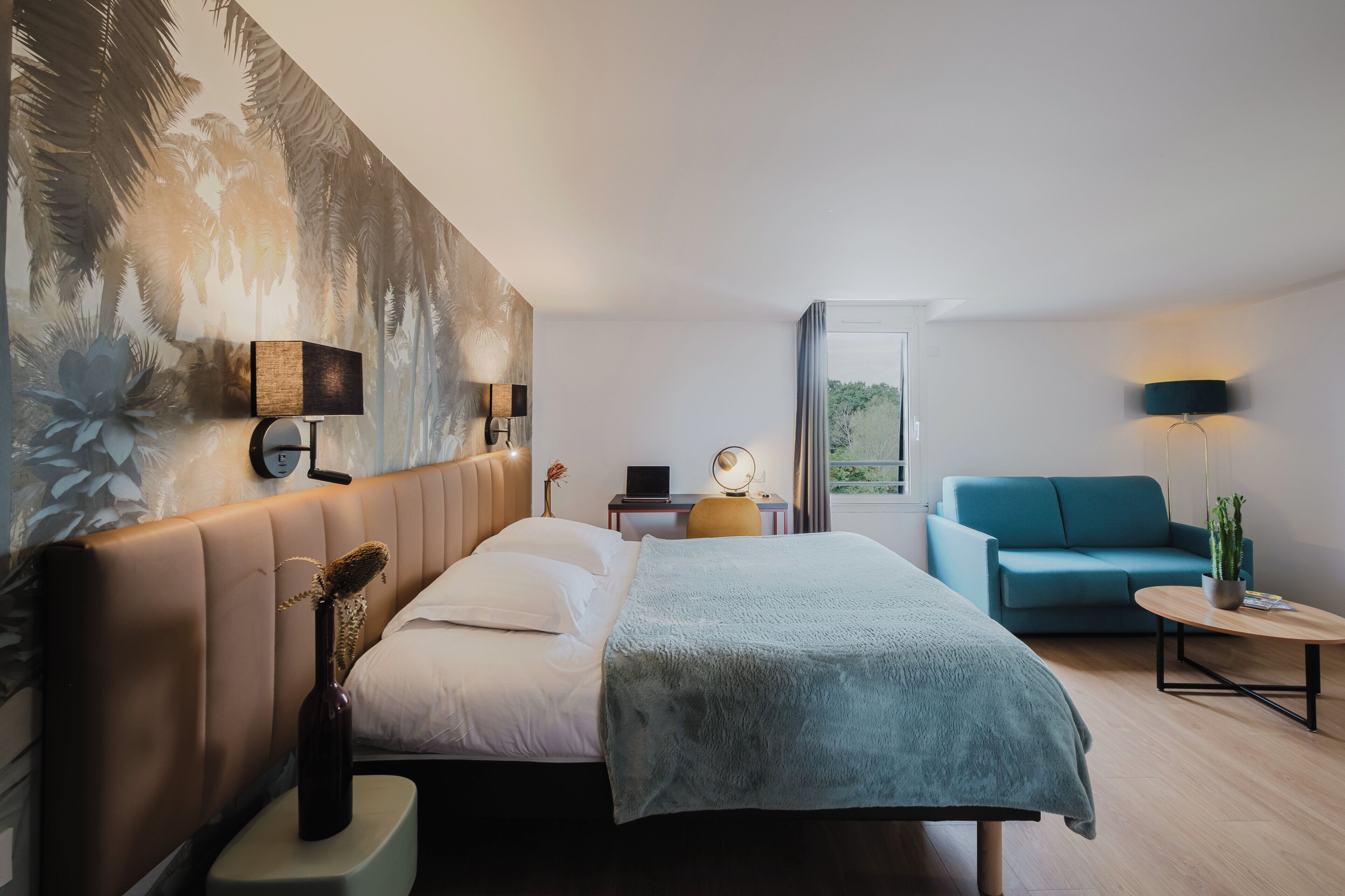 Une chambre d’hôtel moderne dotée d’un grand lit, d’un canapé, d’un bureau avec une lampe et offrant une vue sur l’extérieur.