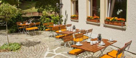 An outdoor patio with tables and chairs, a stone floor, and flower boxes on the building's windowsills.