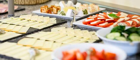 A buffet with various food items including sliced cheese, tomatoes, and cucumbers.