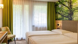 Une chambre d’hôtel avec deux lits, un bureau, une chaise et une grande fresque murale sur le thème de la forêt.