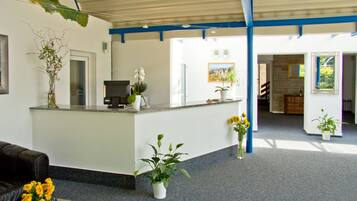 A reception area with a counter, potted plants, a television, and a staircase leading to another room.