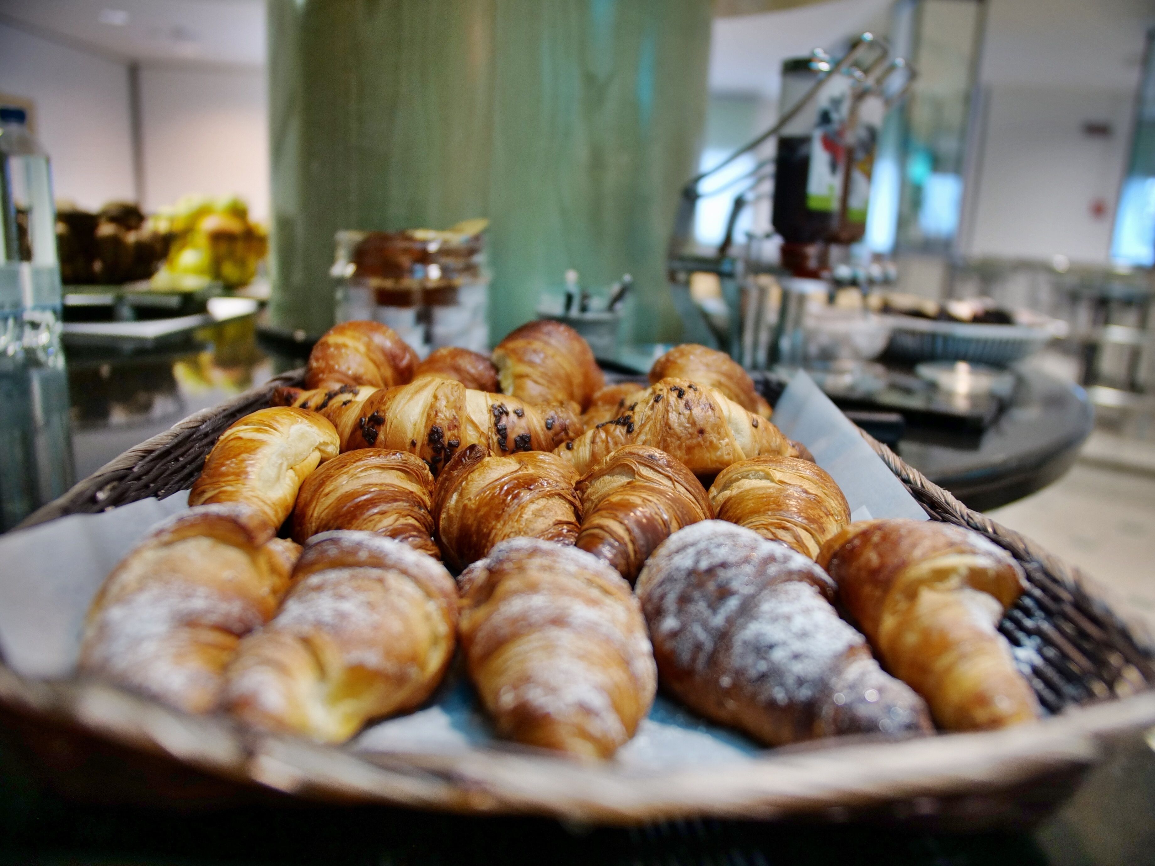A tray of assorted pastries, including croissants and bread rolls, displayed in a buffet setting.