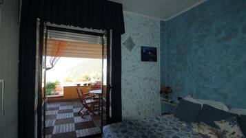 Un dormitorio con cama, mesita de noche, ventana con vistas al exterior y puerta que da a un espacio exterior con mesa y sillas.