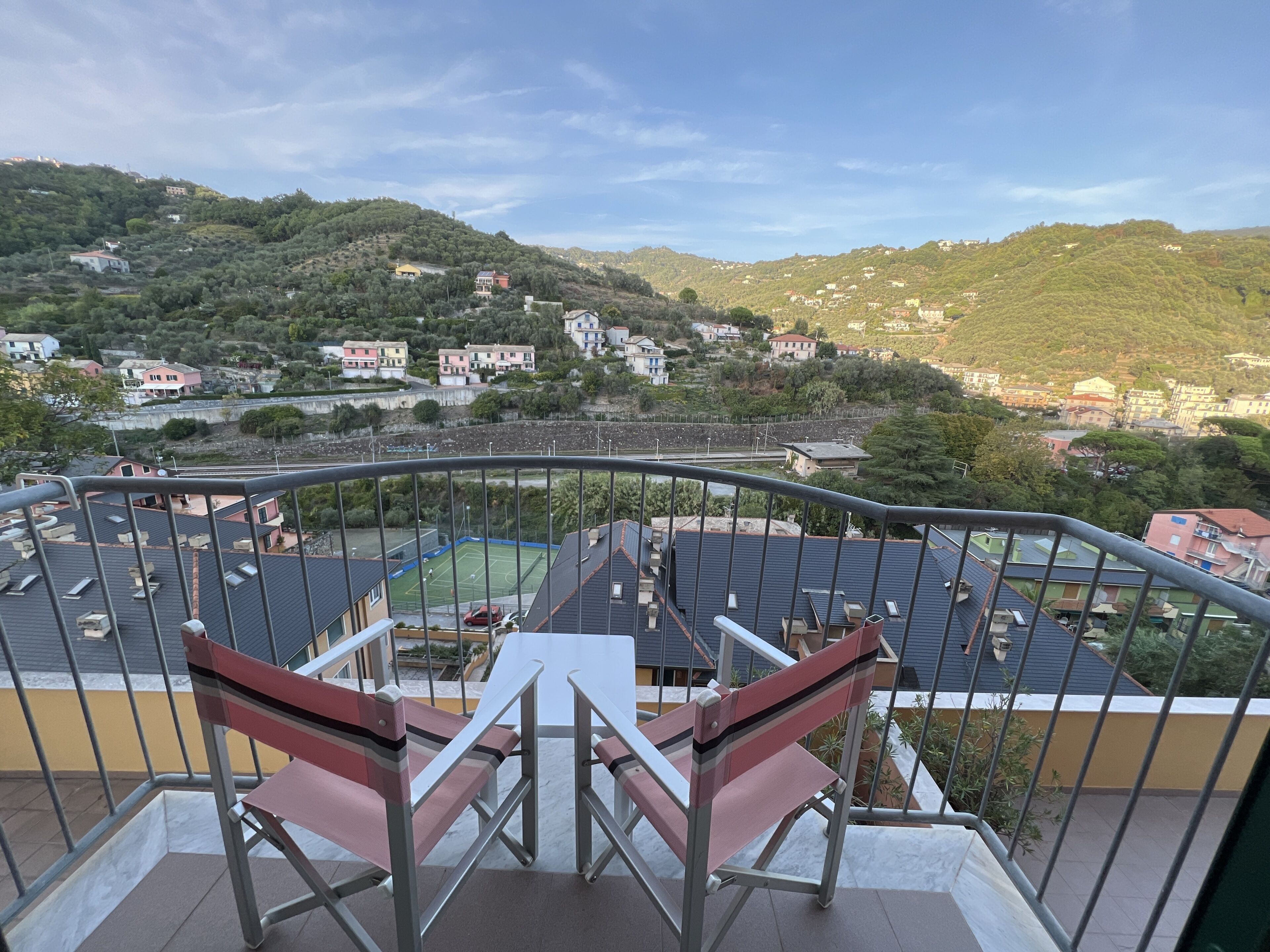 Ein Balkon mit Blick auf einen Tennisplatz, Häuser und Hügel.