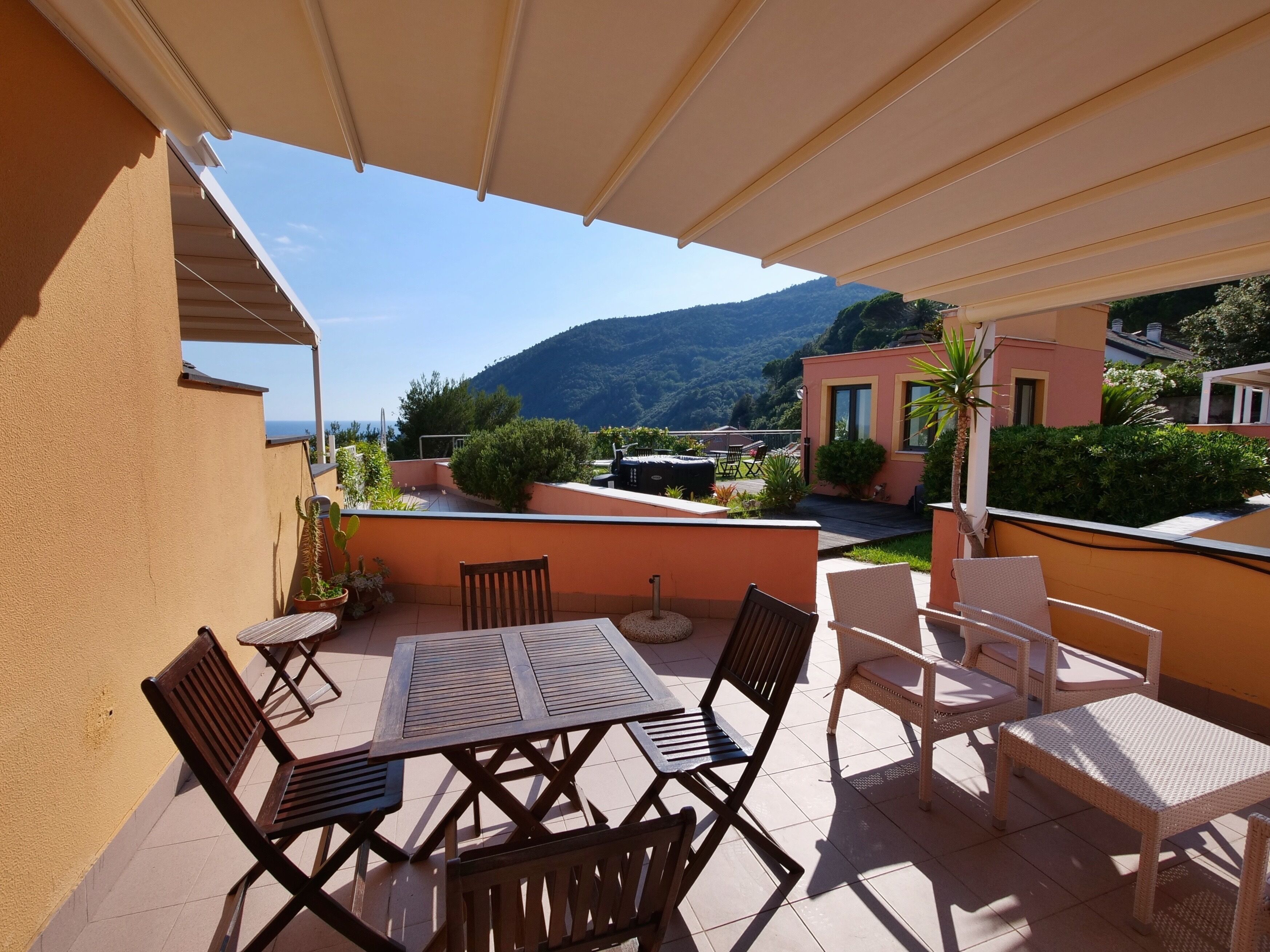Una veranda coperta con tavolo e sedie, vista su una montagna e un edificio sullo sfondo.