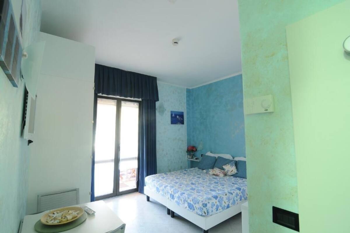 A bedroom with a bed, a window with curtains, a radiator, and a small table with a plate.