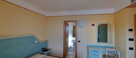 Une chambre à coucher comprenant un lit, un bureau avec une chaise, un miroir et une porte donnant sur une salle de bain.