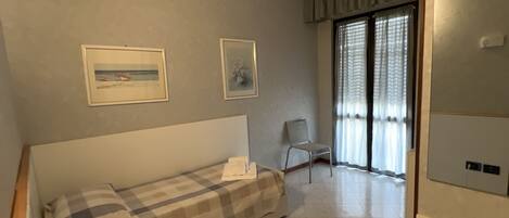 Un dormitorio con cama, una silla, un escritorio con lámpara y un ventanal con cortinas.