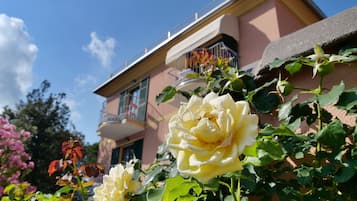Um edifício com varanda e um arbusto de rosas em primeiro plano.
