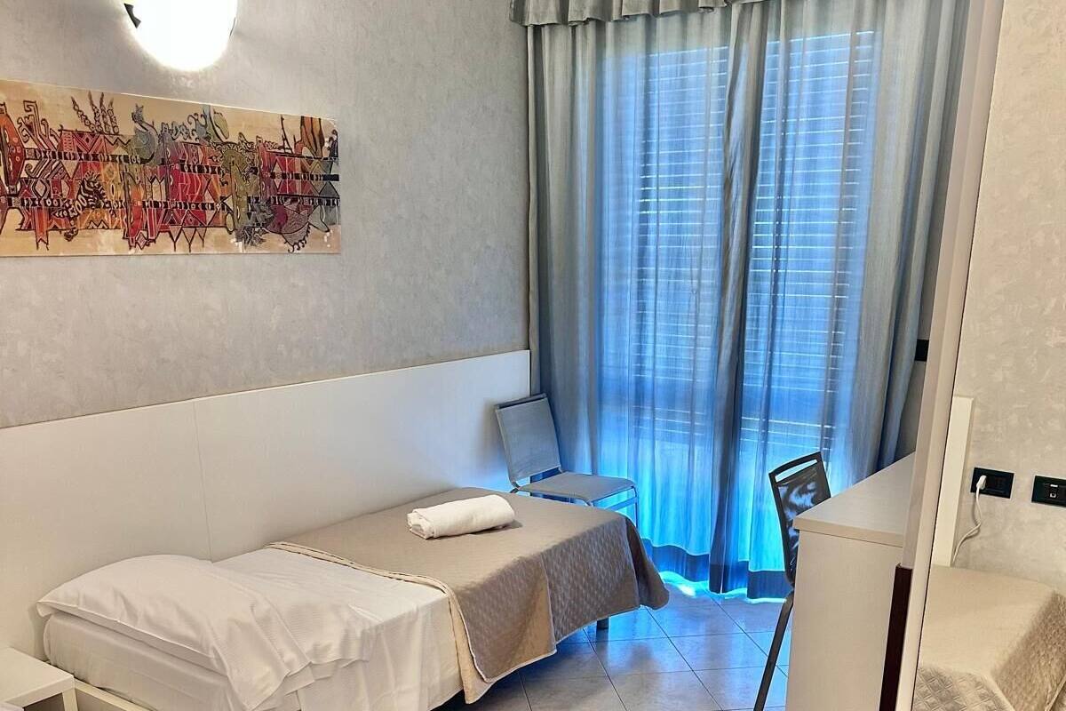 A hotel room with a bed, a chair, a desk, and a window with curtains.