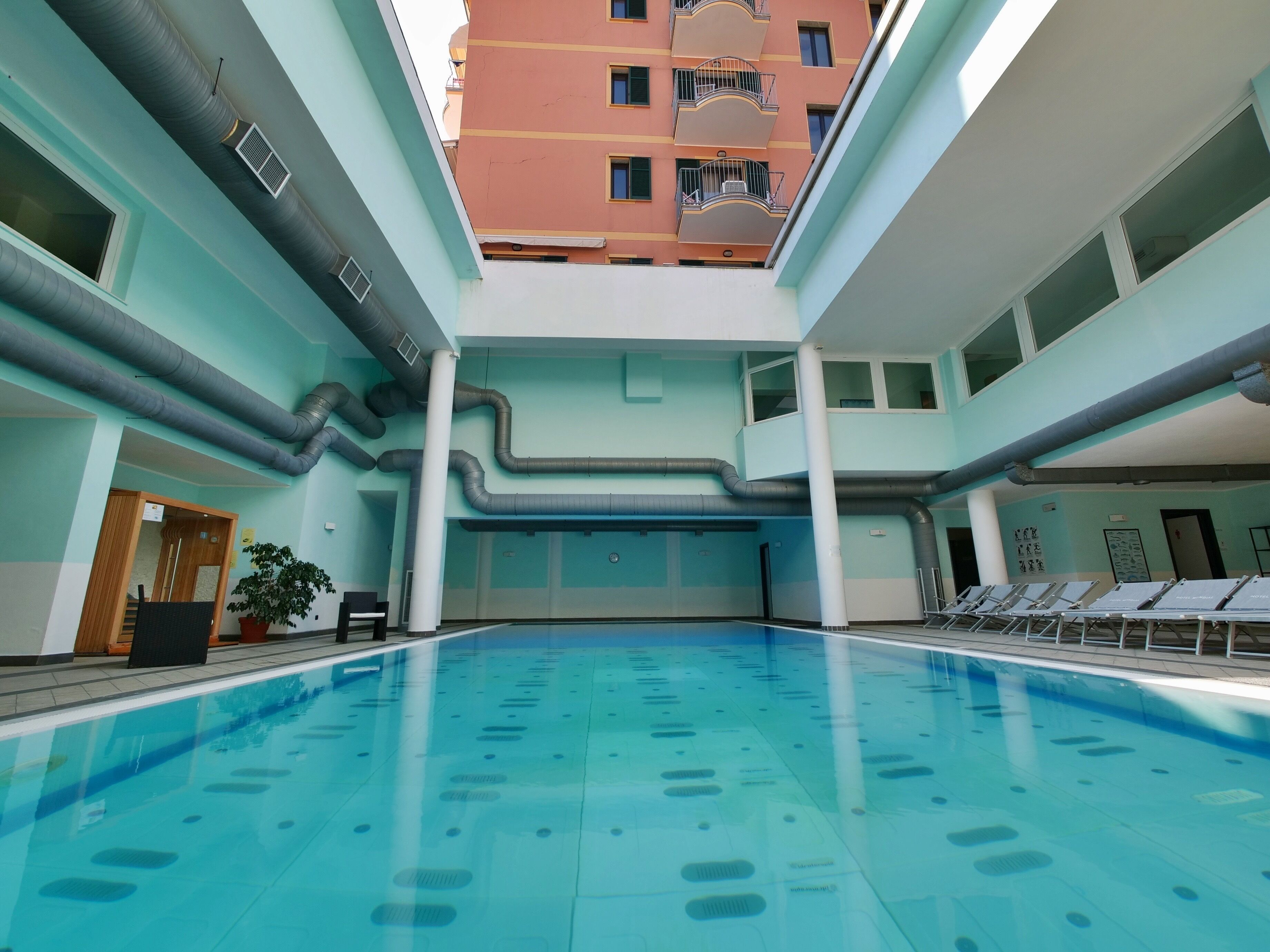 Una piscina con suelo de baldosas, rodeada por muros con ventanas y un balcón.