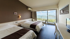 A hotel room with two beds, a desk, a TV, and a balcony with a view of the sea and a plane. - Hotel GranView Garden Okinawa (Tomigusuku)