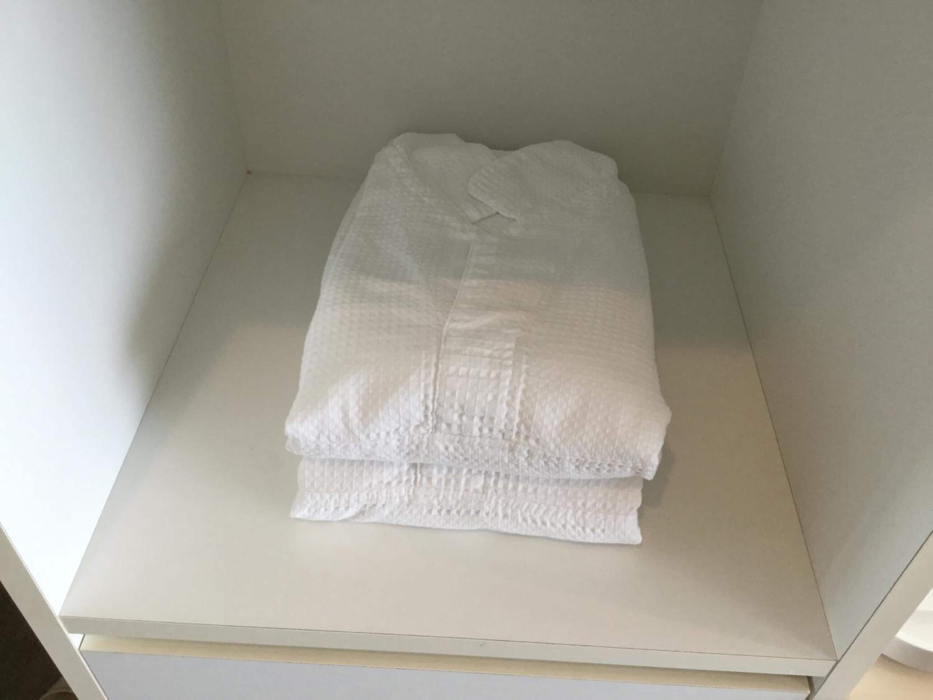 A neatly folded white towel on a white shelf in a room with plain walls.