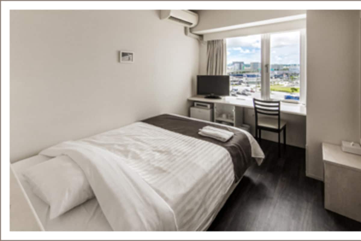 A hotel room with a bed, a desk, a chair, and a window with a city view.