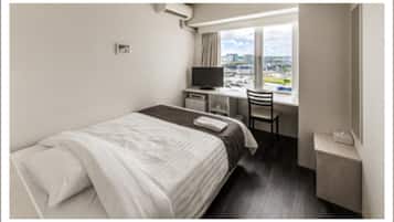 A hotel room with a bed, a desk, a chair, and a window with a city view.
