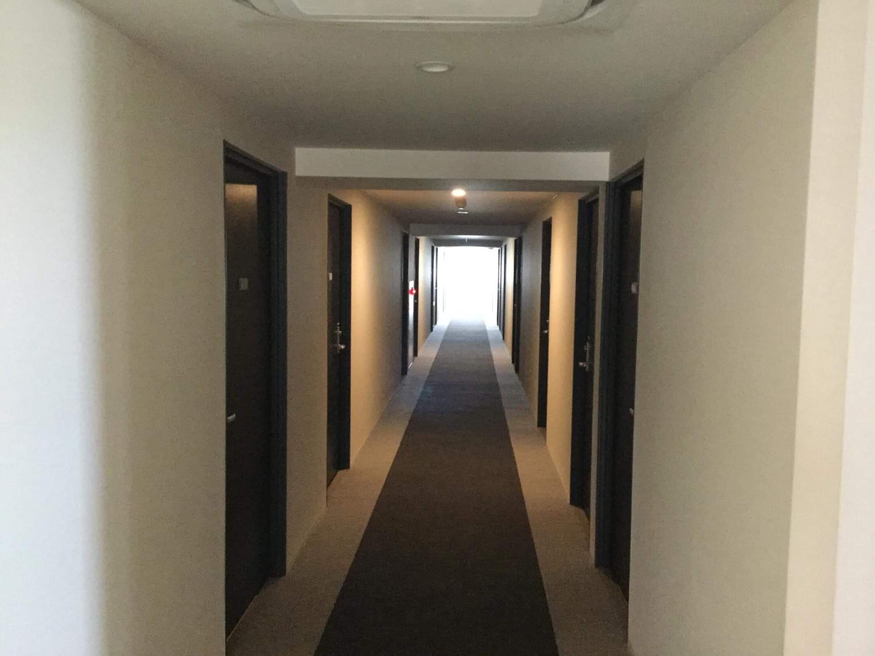 A long, narrow hotel corridor with doors on both sides and a carpeted floor.