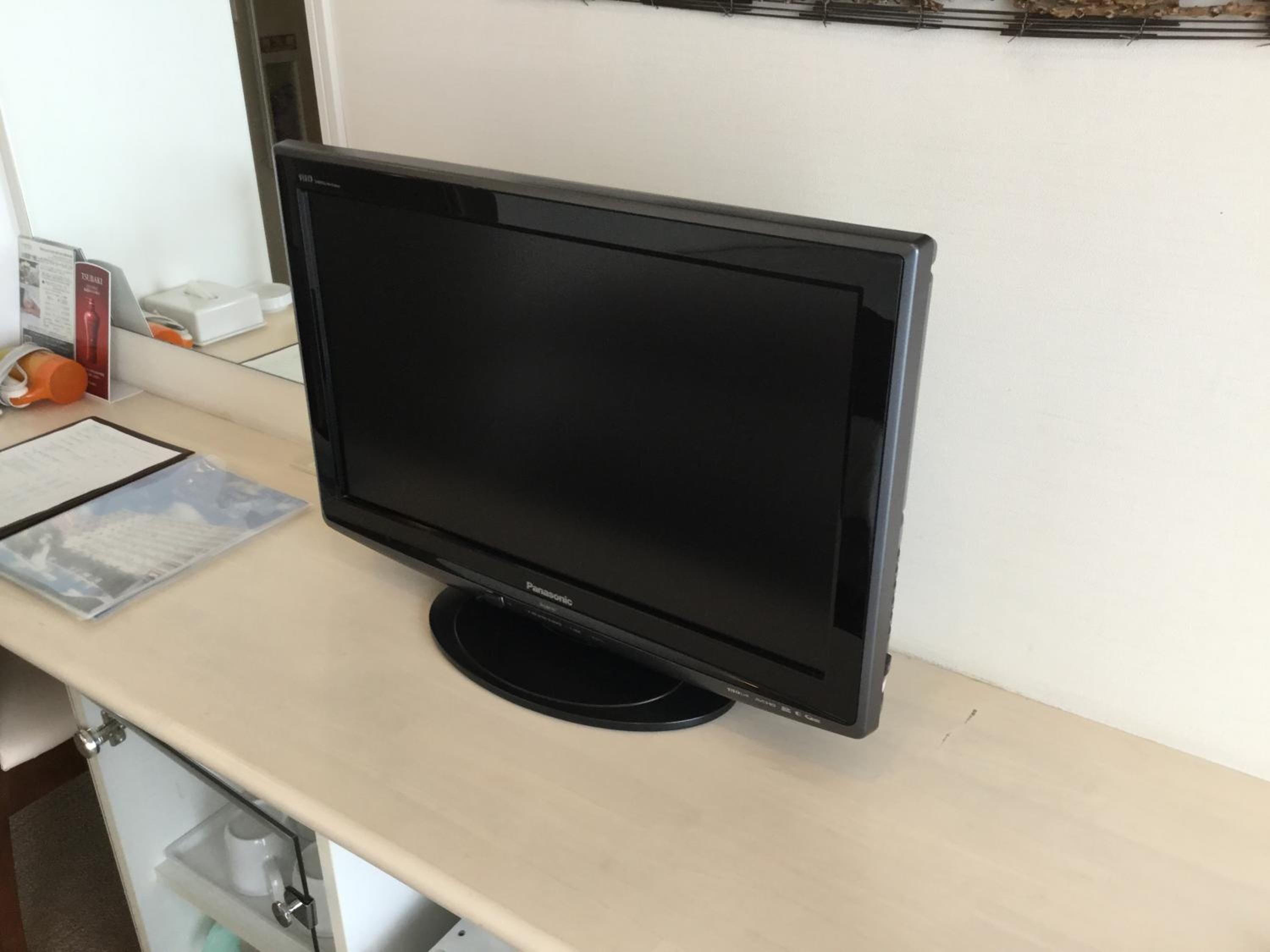 A flat-screen TV on a desk with a document and a small orange object.