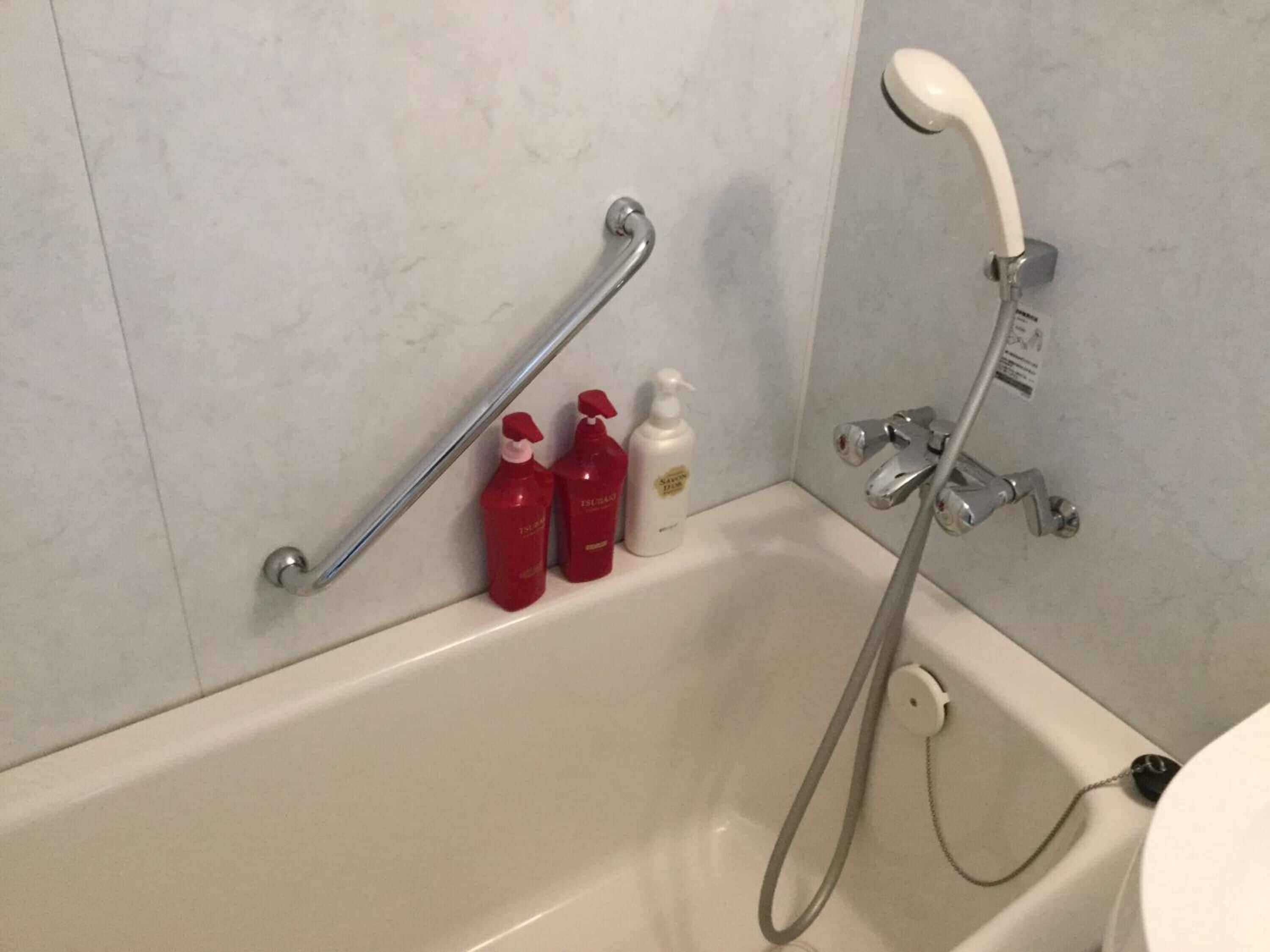 Ein Badezimmer mit einer weißen Badewanne, einer Duschbrause und zwei roten Shampoo-Flaschen an der Wand.