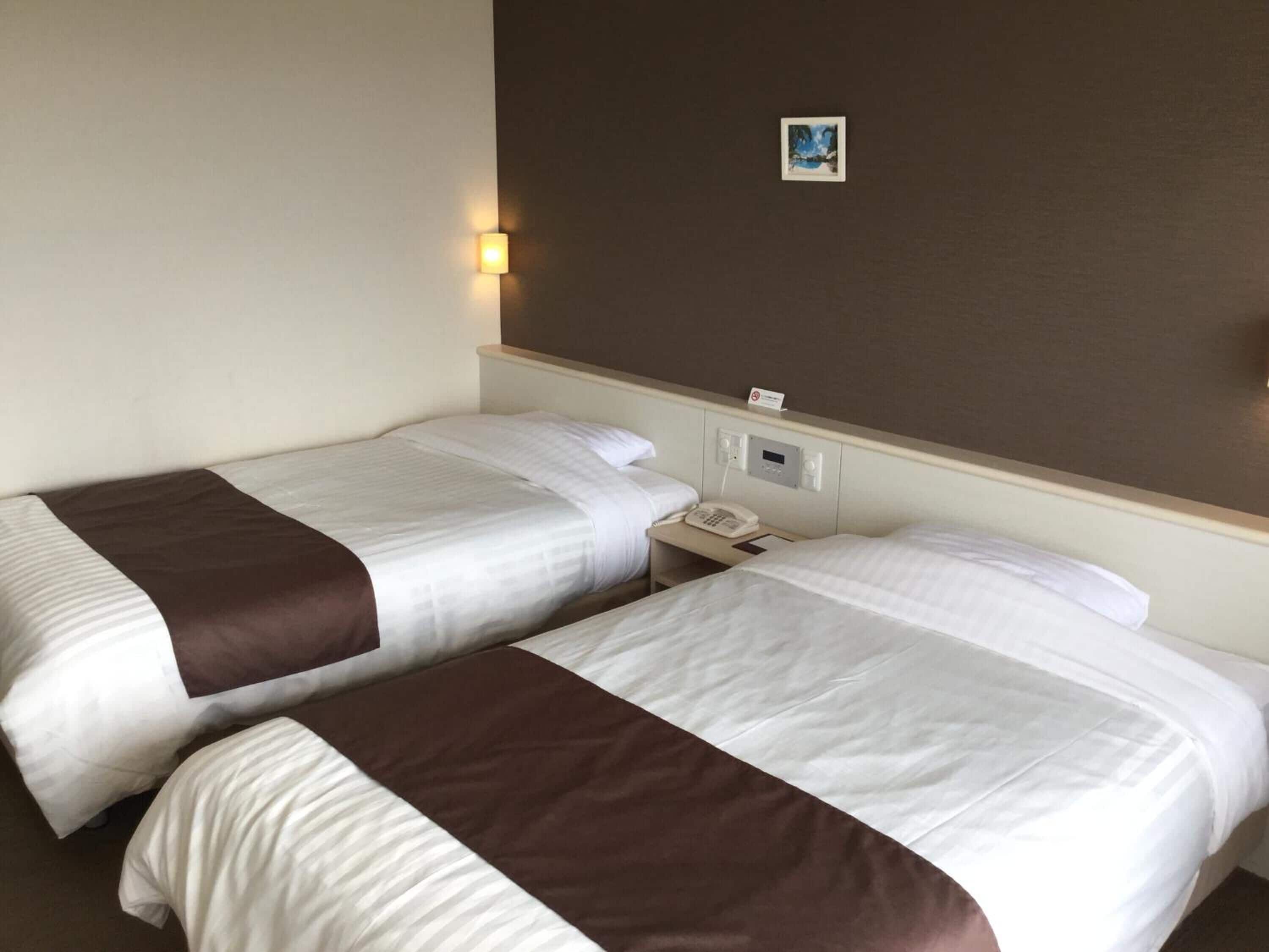 Une chambre d’hôtel avec deux lits, une table de chevet avec un téléphone et une lampe fixée au mur.