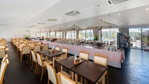 A spacious dining area with long tables and chairs, large windows, and a view of the outdoors. - Hotel GranView Garden Okinawa (Tomigusuku)