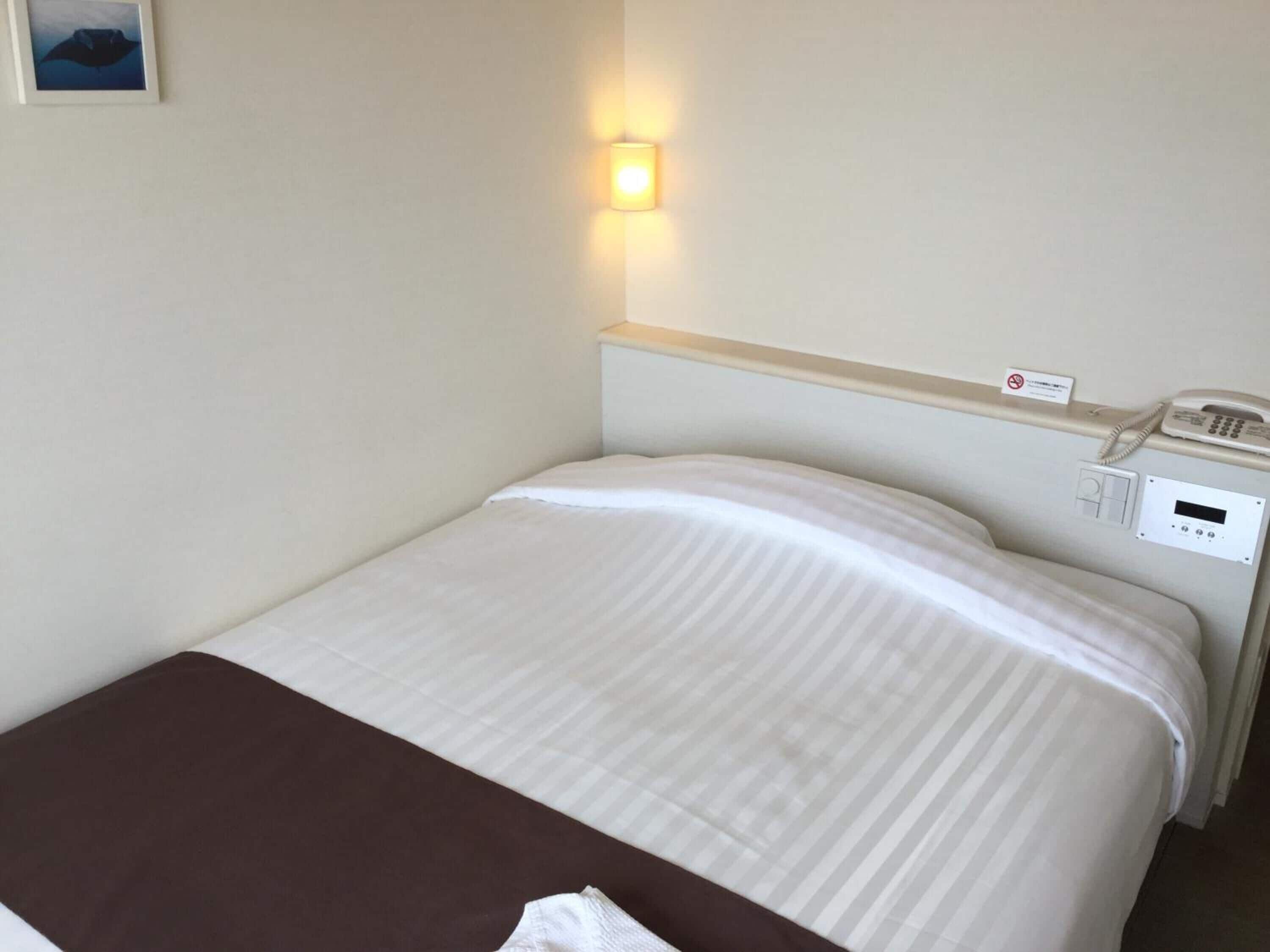 Une chambre d’hôtel équipée d’un lit, d’un téléphone sur la table de chevet, d’une lampe fixée au mur et d’un panneau indiquant qu’il est interdit de fumer.