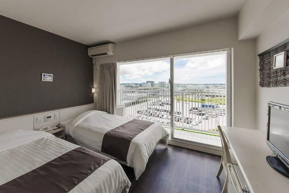 A hotel room with two beds, a TV, and a large window with a city view.