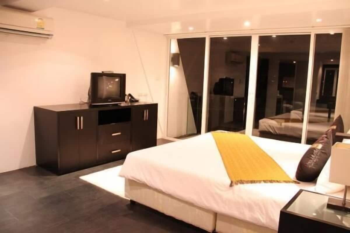 A modern bedroom with a large bed, a dark wooden dresser, and a sliding glass door leading to a balcony.