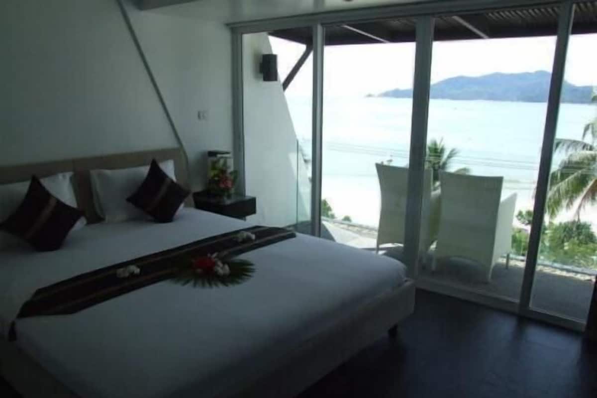 A modern bedroom with a large bed, a nightstand, and a view of the sea.