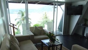 Una sala moderna con sofá, una mesa de centro y televisor. Se observa un ventanal con vistas a palmeras y un edificio.