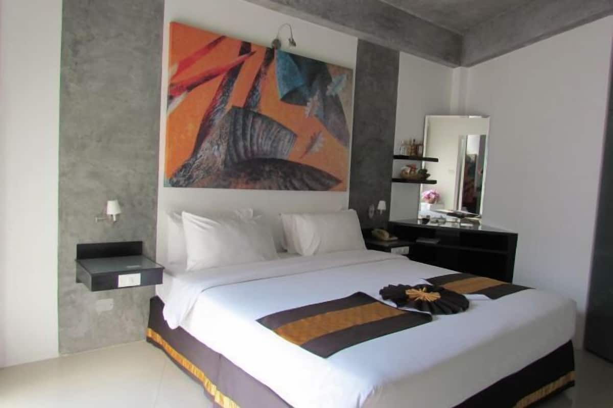 A modern bedroom with a large bed, a bedside table, a nightstand, a mirror, and a colorful abstract painting on the wall.