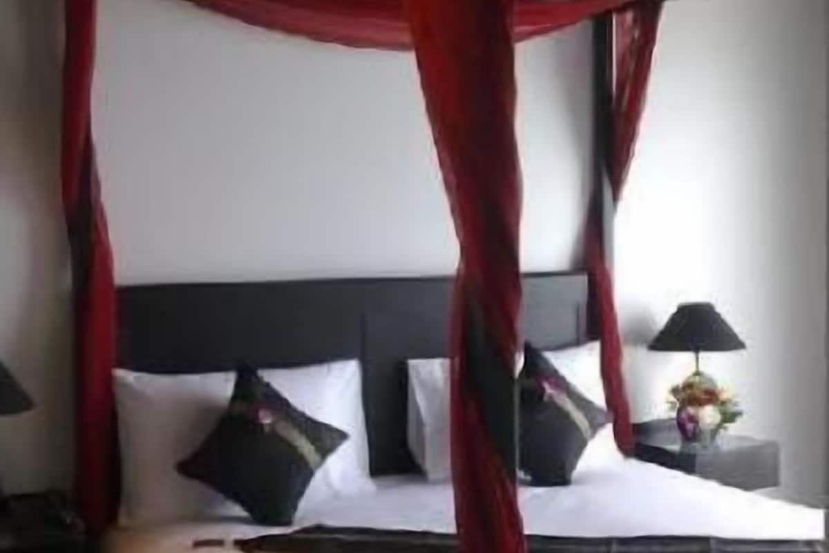 A hotel room with a bed, pillows, a nightstand, a lamp, and a vase with flowers.