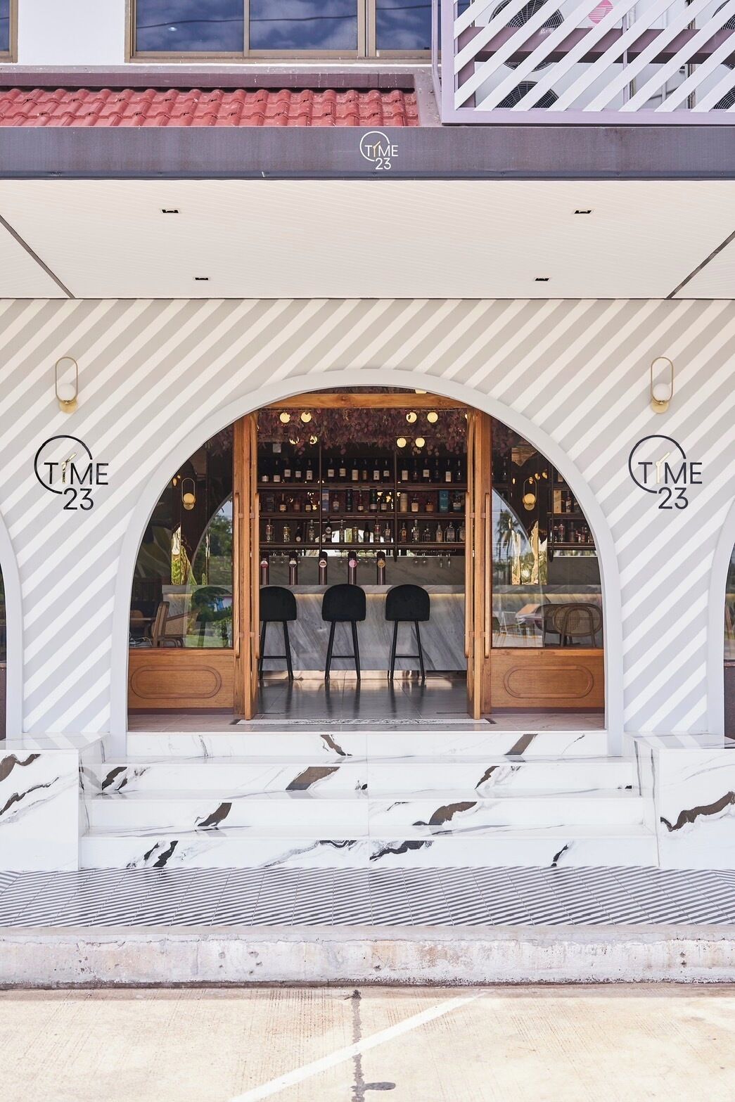 Entrada de un restaurante con diseño moderno, que presenta un arco curvo, una zona de bar con taburetes y una estantería para vinos a la vista.