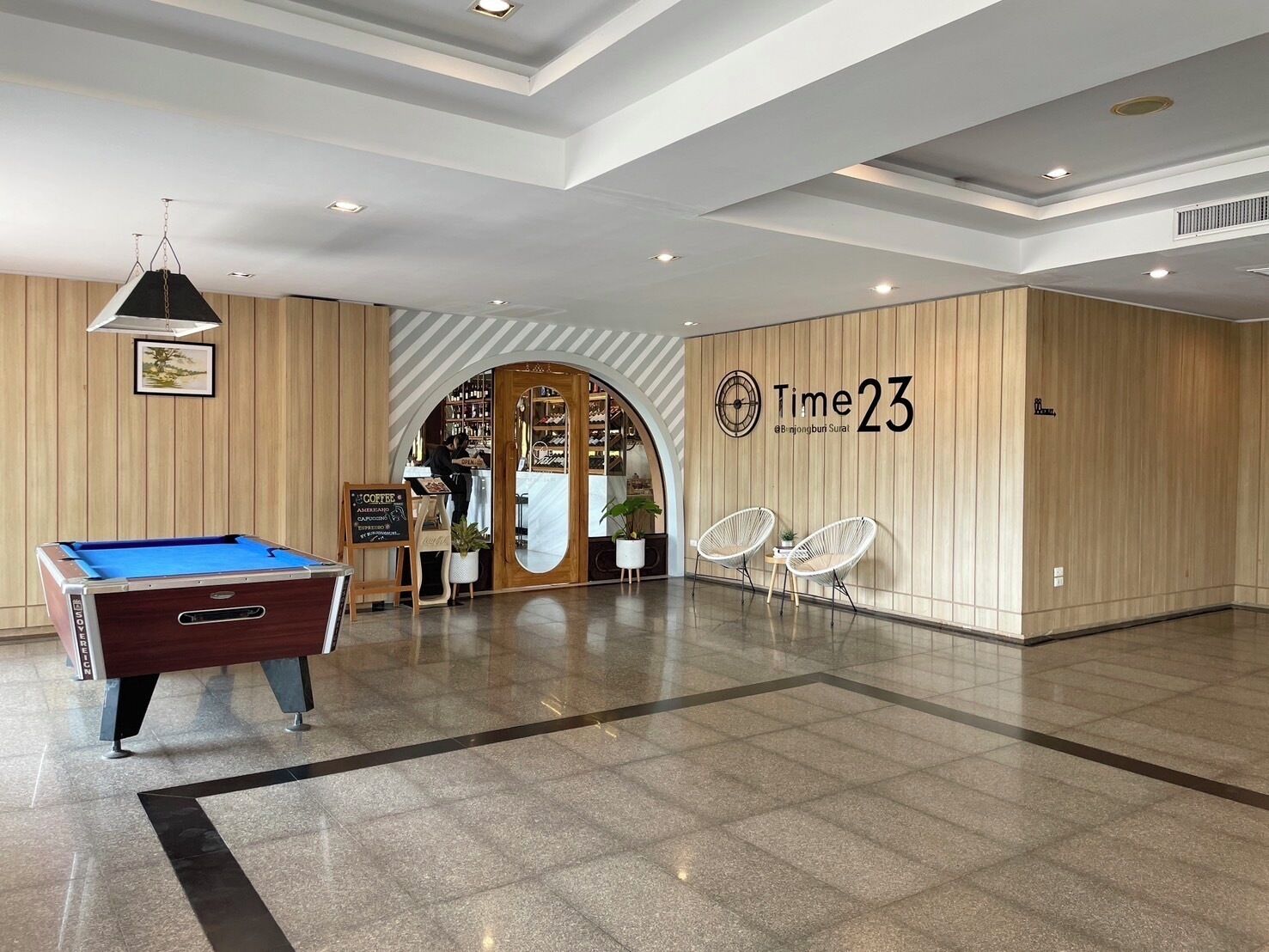 Um lobby moderno com mesa de bilhar, espaço para café e área de recepção com placa indicando "Time 23".