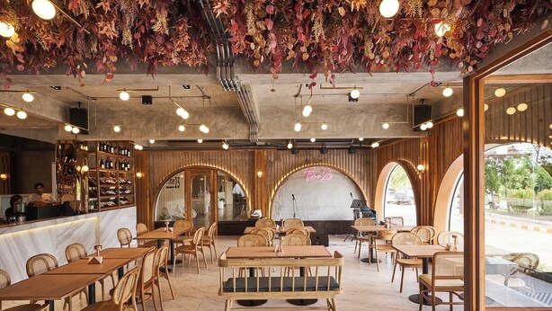 A restaurant interior with wooden tables and chairs, a bar area with wine bottles, and a stage for live music.