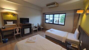 A hotel room with two beds, a desk with a TV, a chair, a window with curtains, and an air conditioning unit.