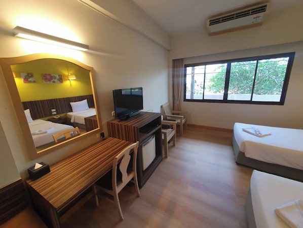 Habitación de hotel con cama, escritorio y silla, televisor, ventana con cortinas y espejo.