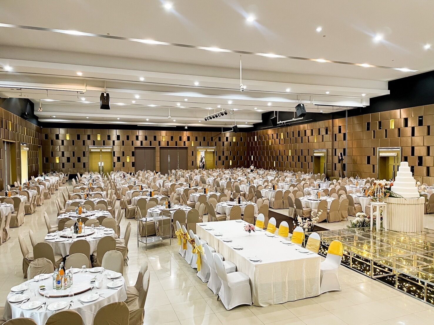 A large banquet hall with round tables and chairs, a stage with a backdrop, and a decorative centerpiece.