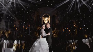 A couple embracing at a wedding reception with a chandelier and ornate decorations.