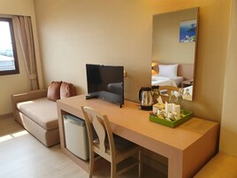 Habitación de hotel con cama, escritorio, silla, refrigerador pequeño, televisión y espejo.