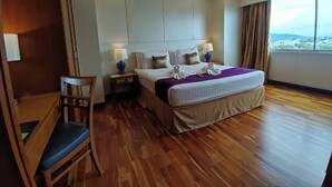 Hotelkamer met een groot bed, houten vloer, een bureau met stoel en een raam met uitzicht.