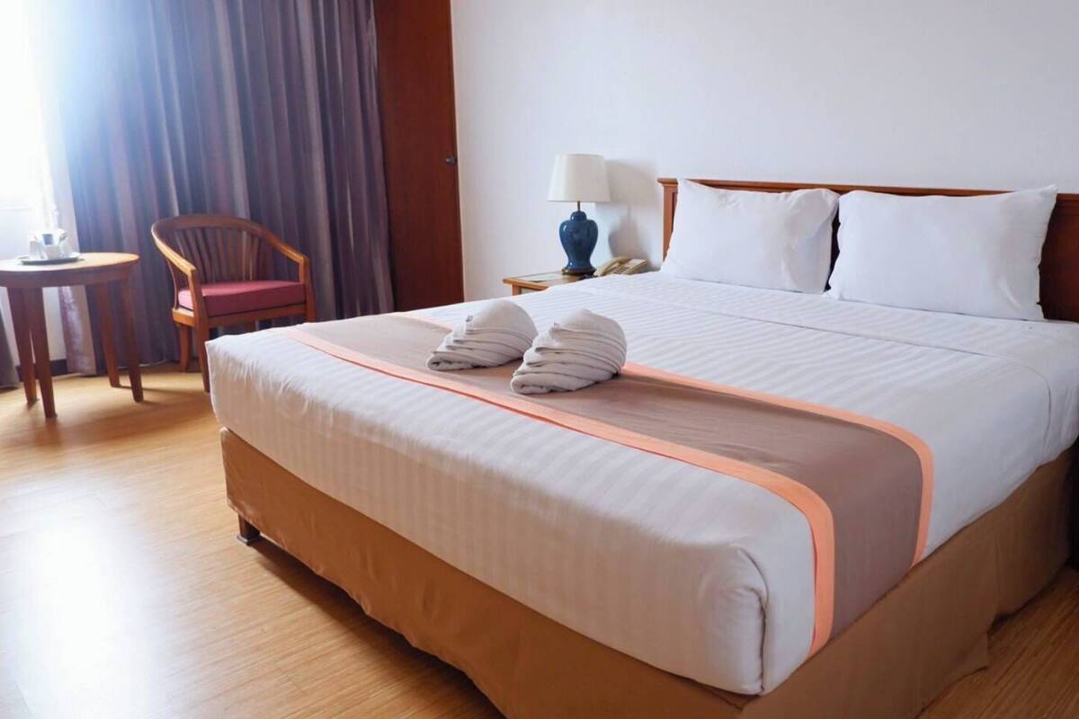 Een hotelkamer met een groot bed, een stoel, een nachtkastje en een lamp.