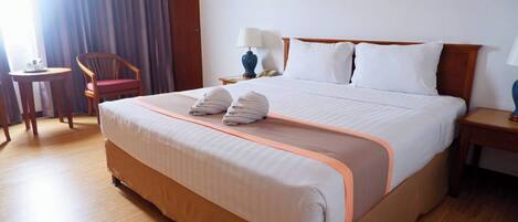 A hotel room with a large bed, a chair, a nightstand, and a lamp.