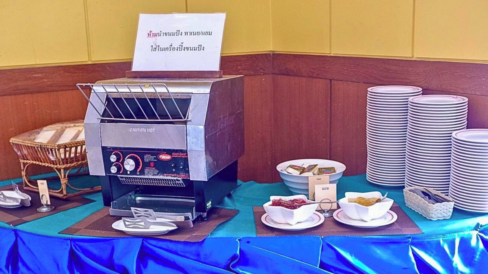 Disposición de un bufé con una máquina de café, platos, tazones y un cartel que indica bebidas calientes.