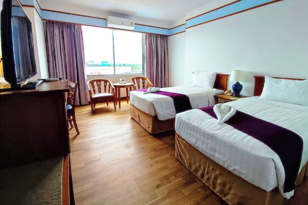 Een hotelkamer met twee bedden, een bureau, een stoel, een televisie en een raam met gordijnen.